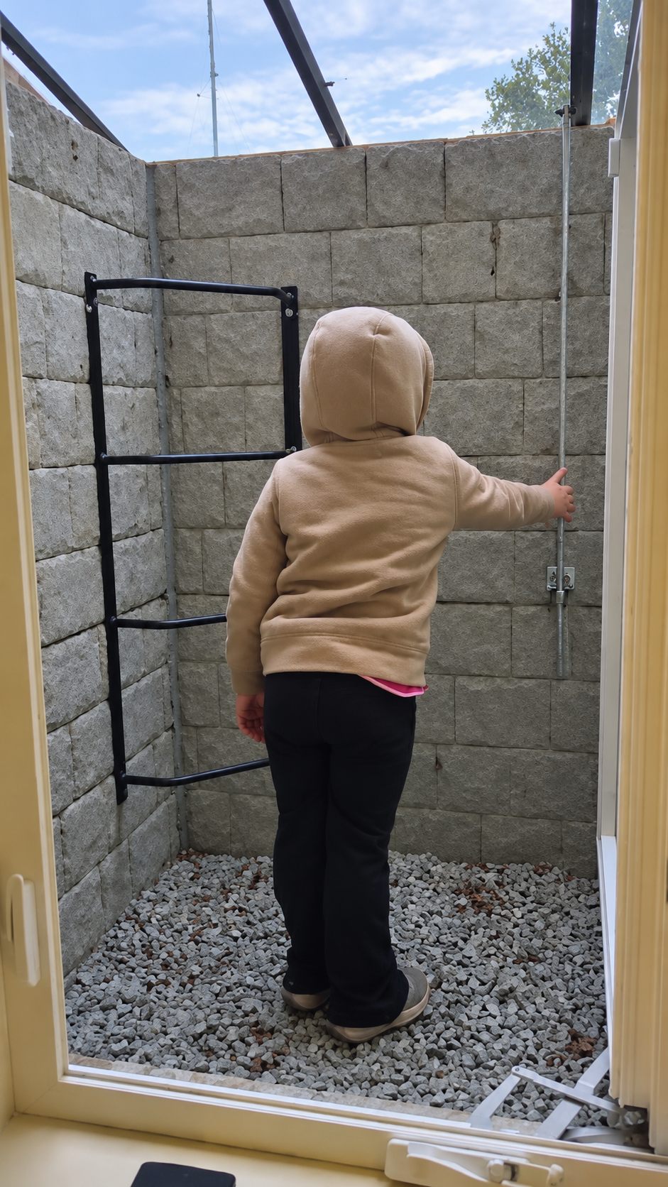 Young girl standing in a concrete egress window well, reaching for the cover release