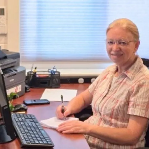 Ann Schrag writing at her desk looking at the camera